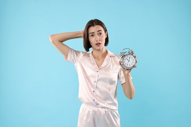 Overslept young woman with alarm clock on light blue background