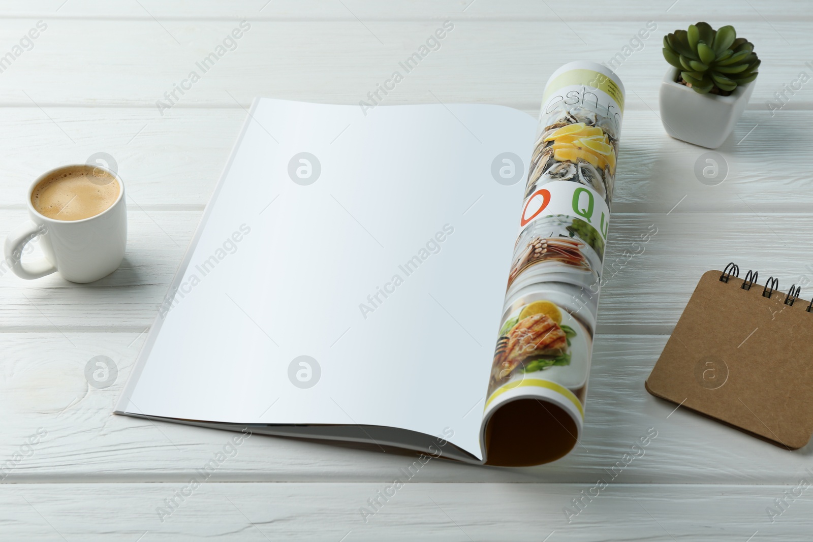 Photo of Open magazine with blank page, coffee, plant and notebook on white wooden table. Mockup for design