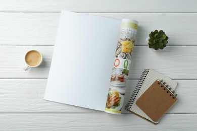 Open magazine with blank page, coffee, plant and notebooks on white wooden table, flat lay. Mockup for design