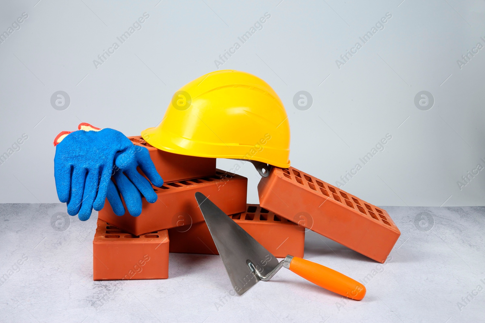 Photo of Red bricks, trowel, gloves and hardhat on textured table against light background