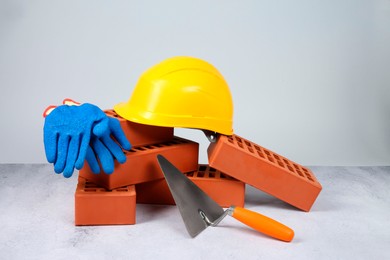 Photo of Red bricks, trowel, gloves and hardhat on textured table against light background