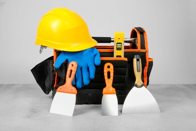 Bag for construction tools, building level, hard hat, glove and trowels on textured table against light background