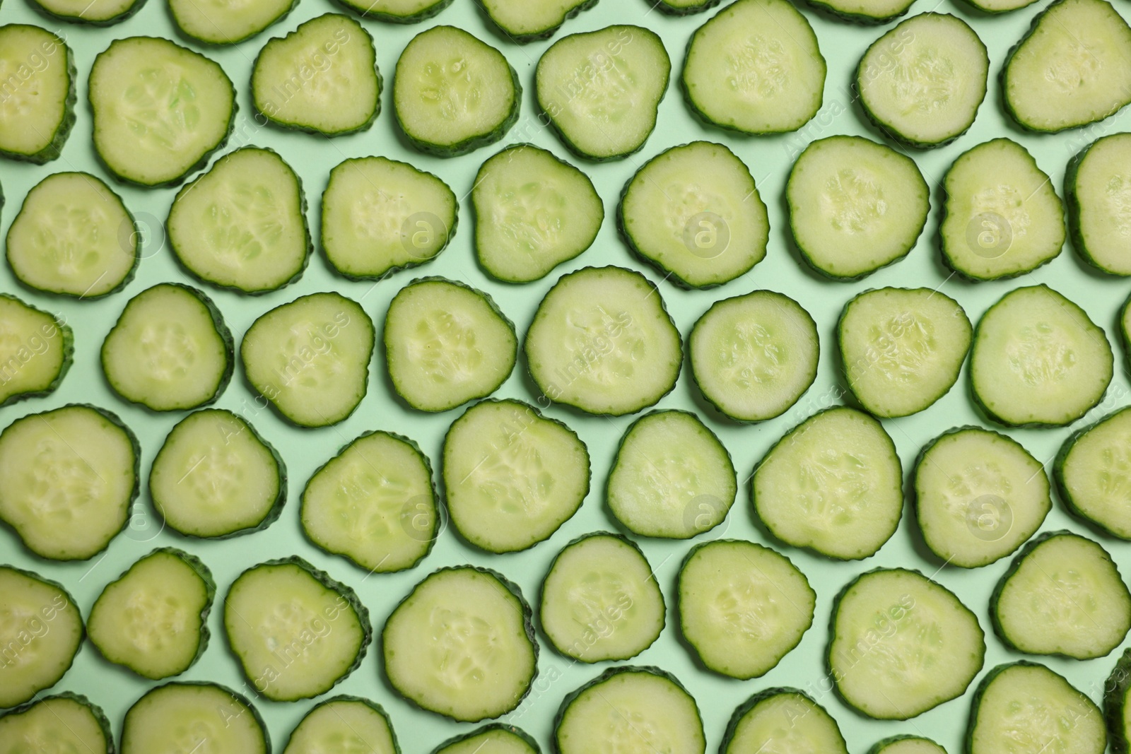 Photo of Slices of fresh cucumbers on turquoise background, flat lay