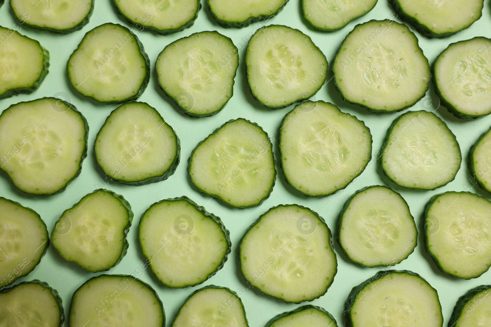 Photo of Slices of fresh cucumbers on turquoise background, flat lay