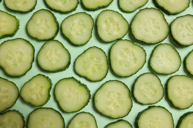 Photo of Slices of fresh cucumbers on turquoise background, flat lay