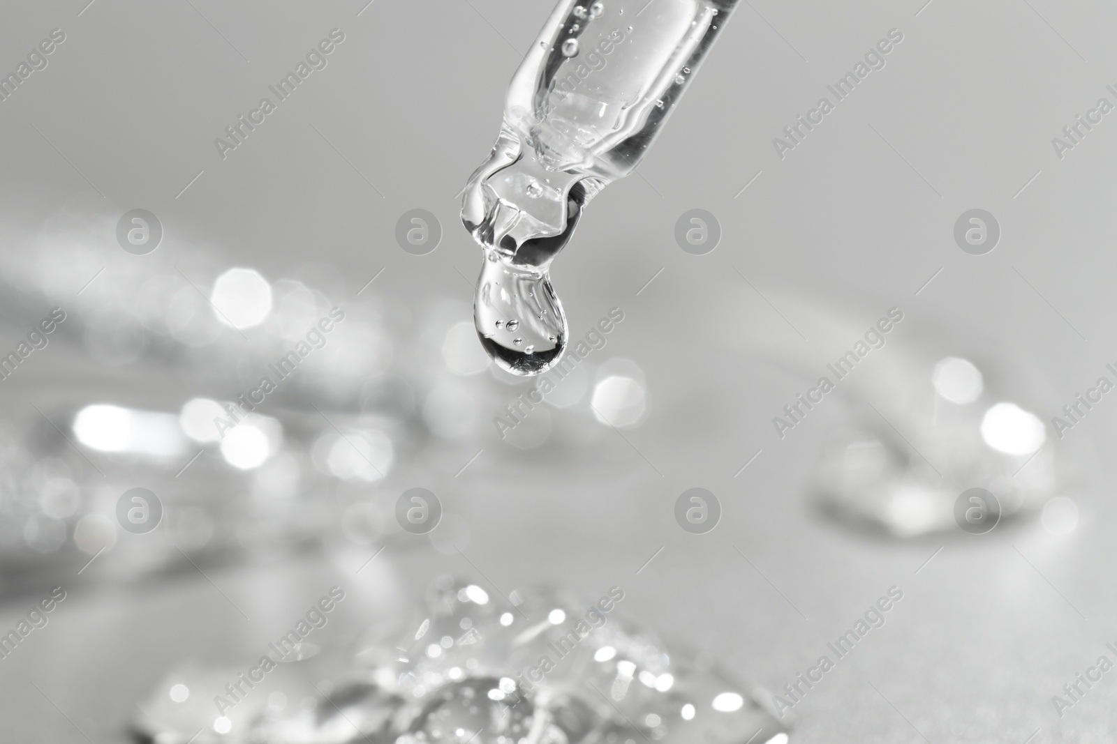 Photo of Dripping cosmetic serum from pipette on grey background, closeup