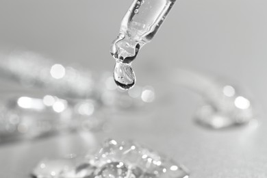 Dripping cosmetic serum from pipette on grey background, closeup