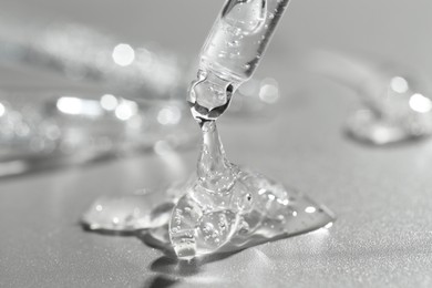 Photo of Dripping cosmetic serum from pipette on grey background, closeup