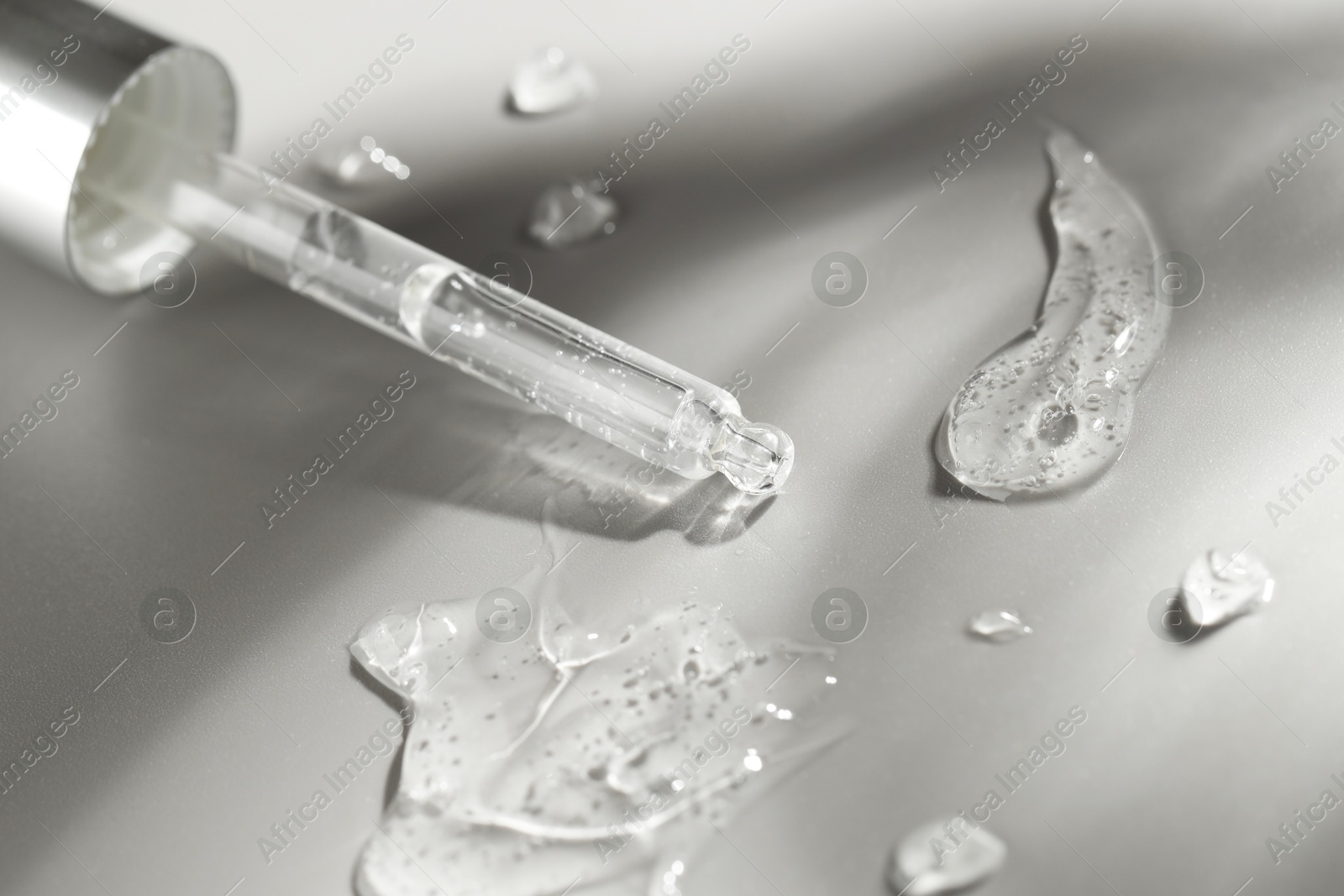 Photo of Dripping cosmetic serum from pipette on grey background