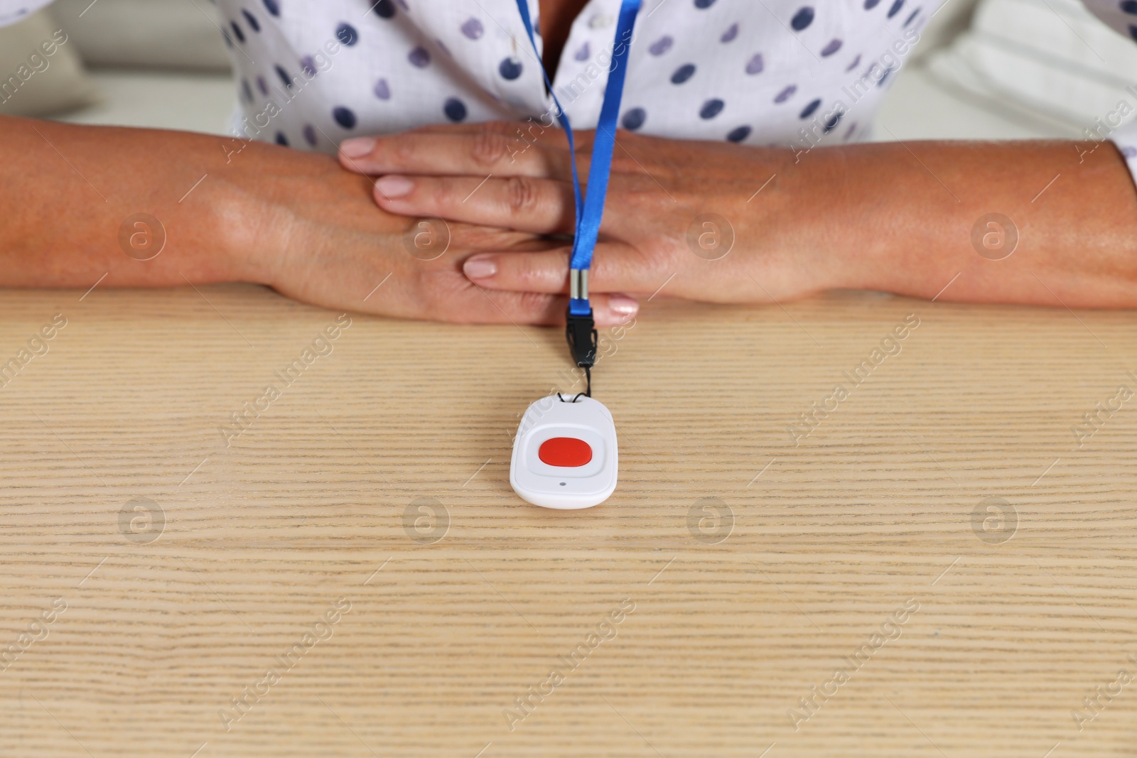 Photo of Senior woman with emergency call button at wooden table, closeup