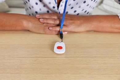 Photo of Senior woman with emergency call button at wooden table, closeup