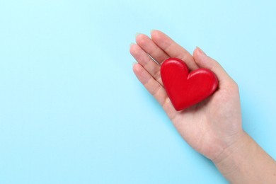 Woman with red heart on light blue background, top view. Space for text