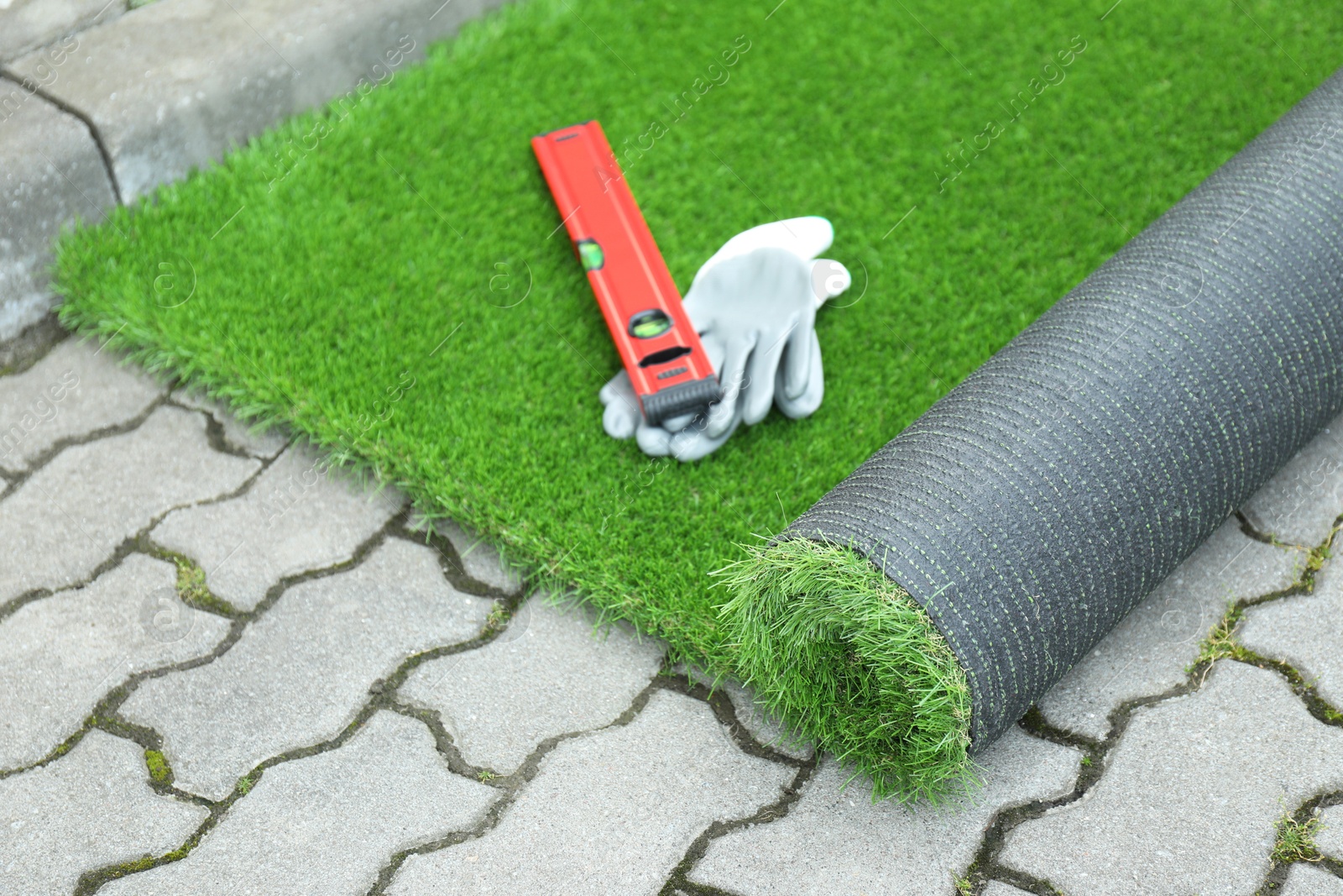 Photo of Gloves, level tool and roll of artificial turf outdoors