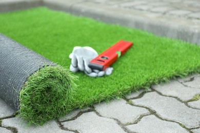 Gloves, level tool and roll of artificial turf outdoors, closeup