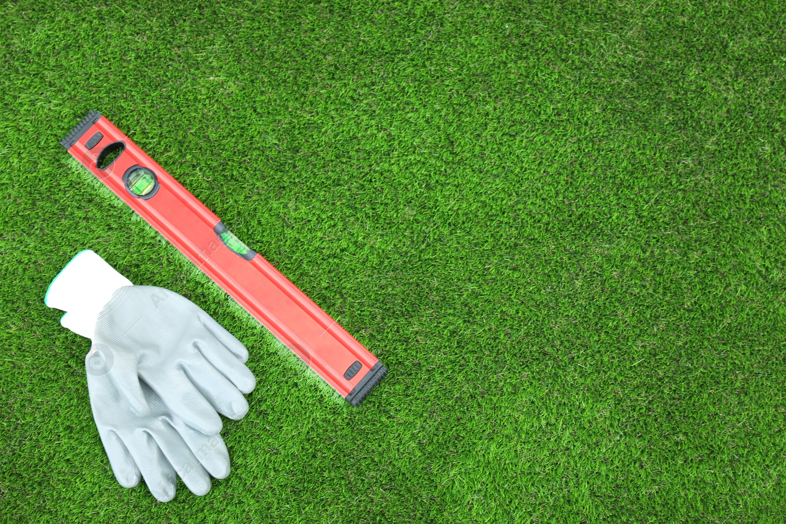 Photo of Gloves and level tool on artificial turf, top view