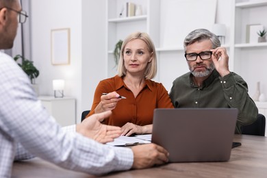 Pension plan. Couple consulting with insurance agent at table indoors