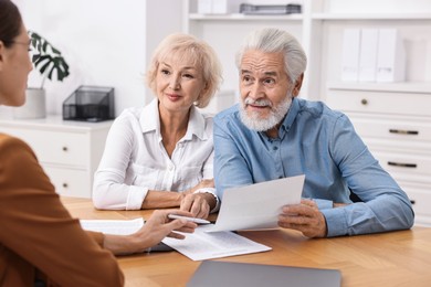 Pension plan. Senior couple consulting with insurance agent at wooden table indoors