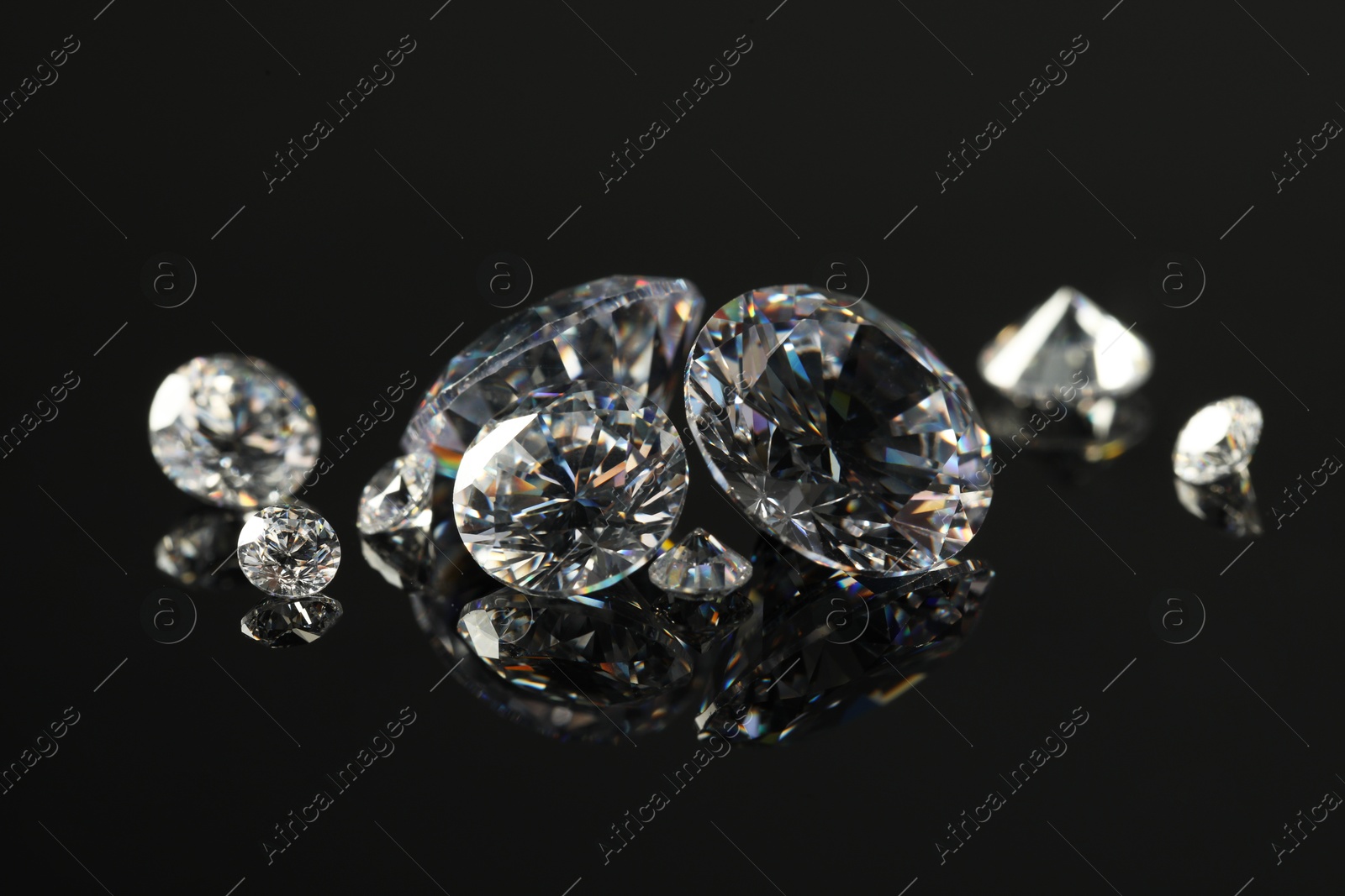 Photo of Many beautiful shiny diamonds on black mirror surface, closeup