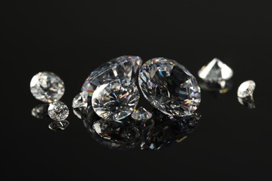 Photo of Many beautiful shiny diamonds on black mirror surface, closeup