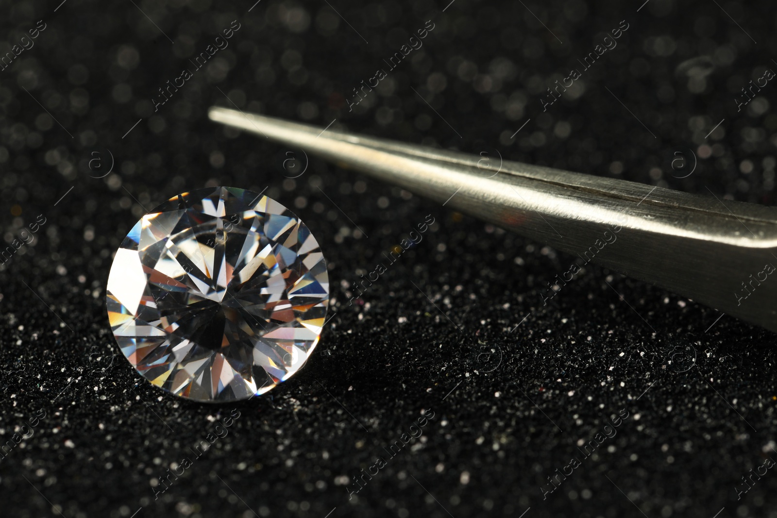 Photo of Beautiful dazzling diamond and tweezers on dark shiny background, closeup