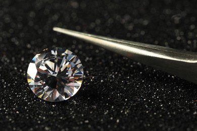 Photo of Beautiful dazzling diamond and tweezers on dark shiny background, closeup