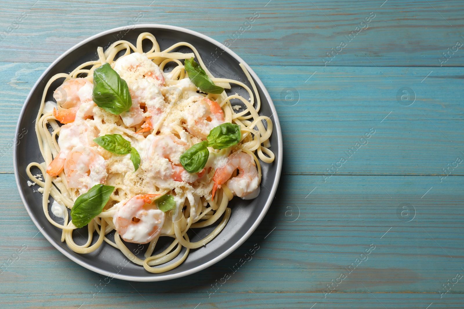 Photo of Tasty pasta with shrimps on light blue wooden table, top view. Space for text