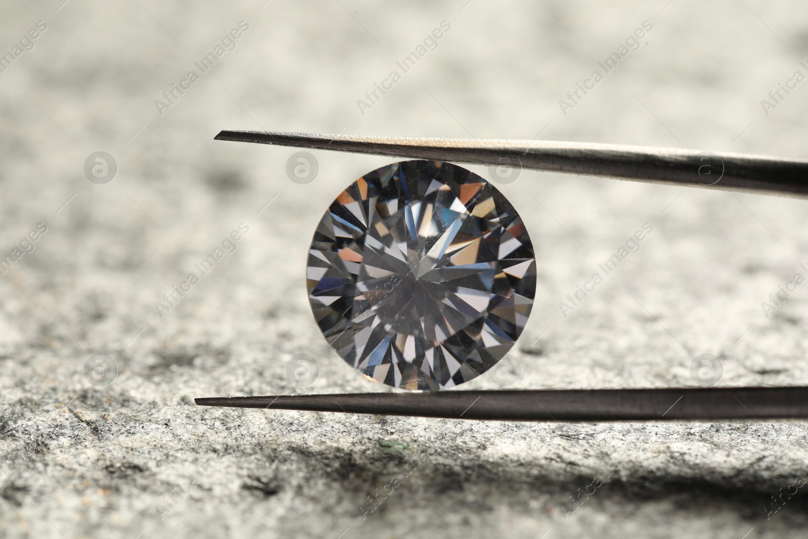 Photo of Beautiful shiny diamond and tweezers on grey textured table, closeup