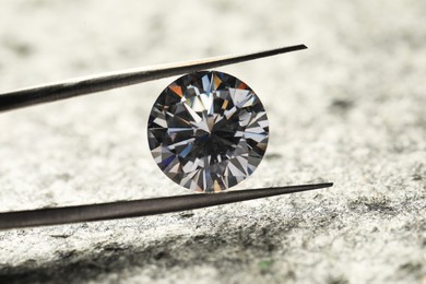 Photo of Beautiful shiny diamond and tweezers on grey textured table, closeup