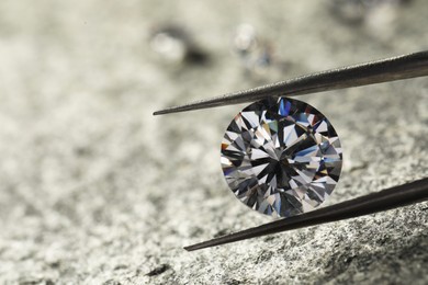 Photo of Beautiful shiny diamond and tweezers on grey textured table, closeup. Space for text