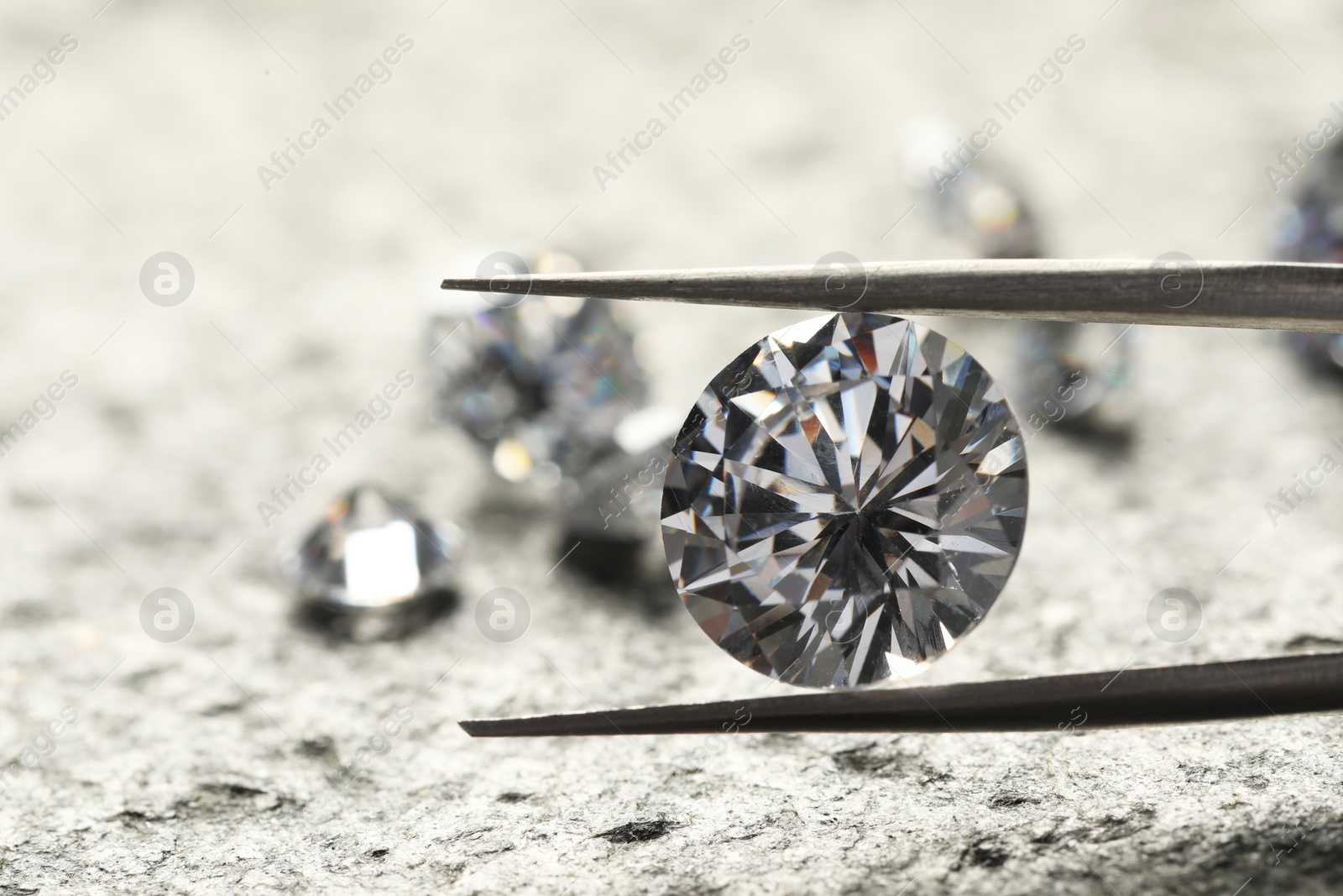 Photo of Many beautiful shiny diamonds and tweezers on grey textured table, closeup