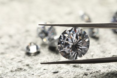 Photo of Many beautiful shiny diamonds and tweezers on grey textured table, closeup