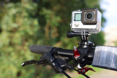 Photo of Modern action camera with mount on bicycle outdoors, space for text