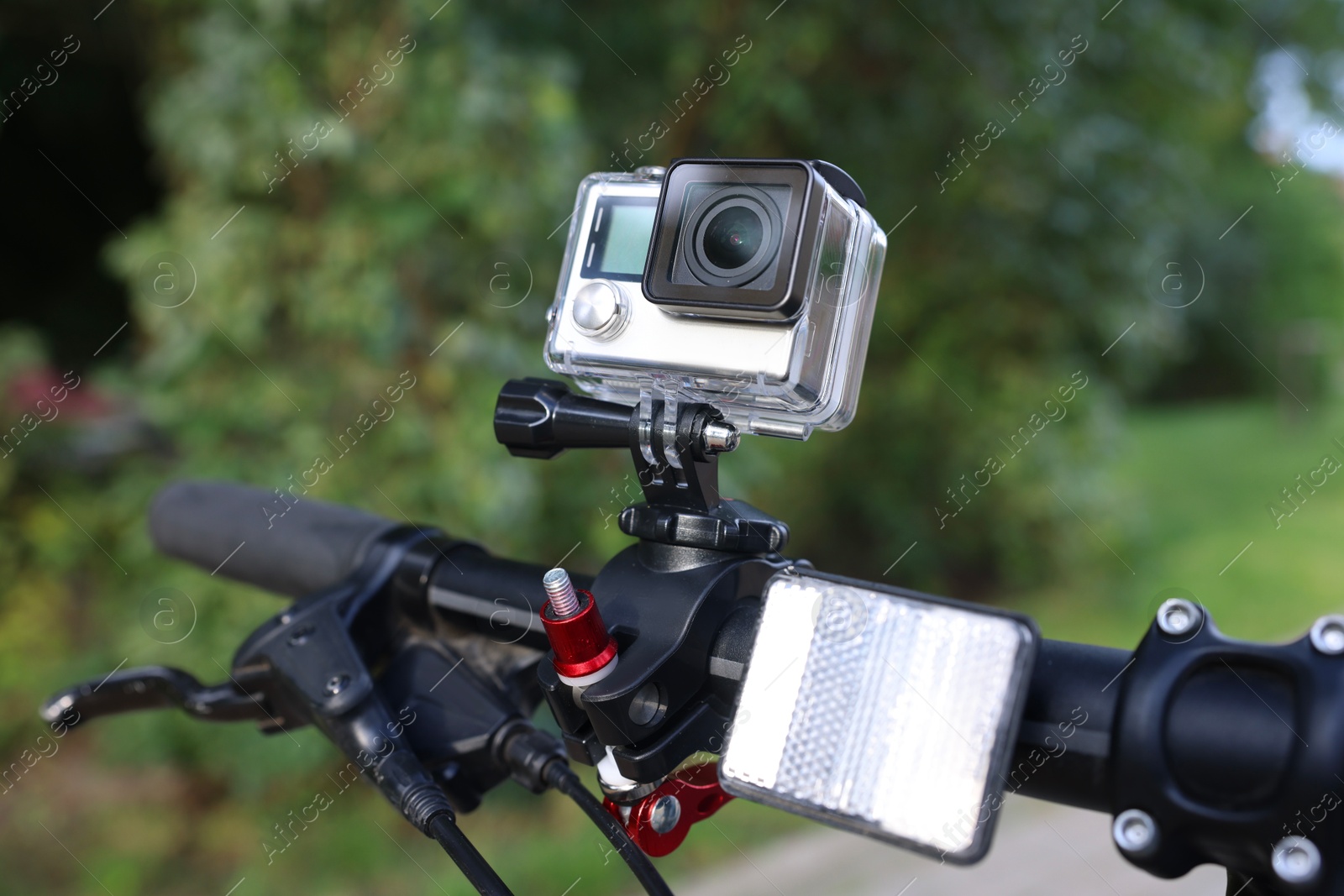 Photo of Modern action camera with mount on bicycle outdoors, closeup