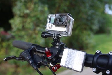 Photo of Modern action camera with mount on bicycle outdoors, closeup