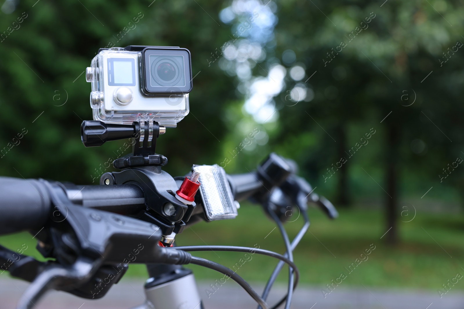 Photo of Modern action camera with mount on bicycle outdoors, space for text