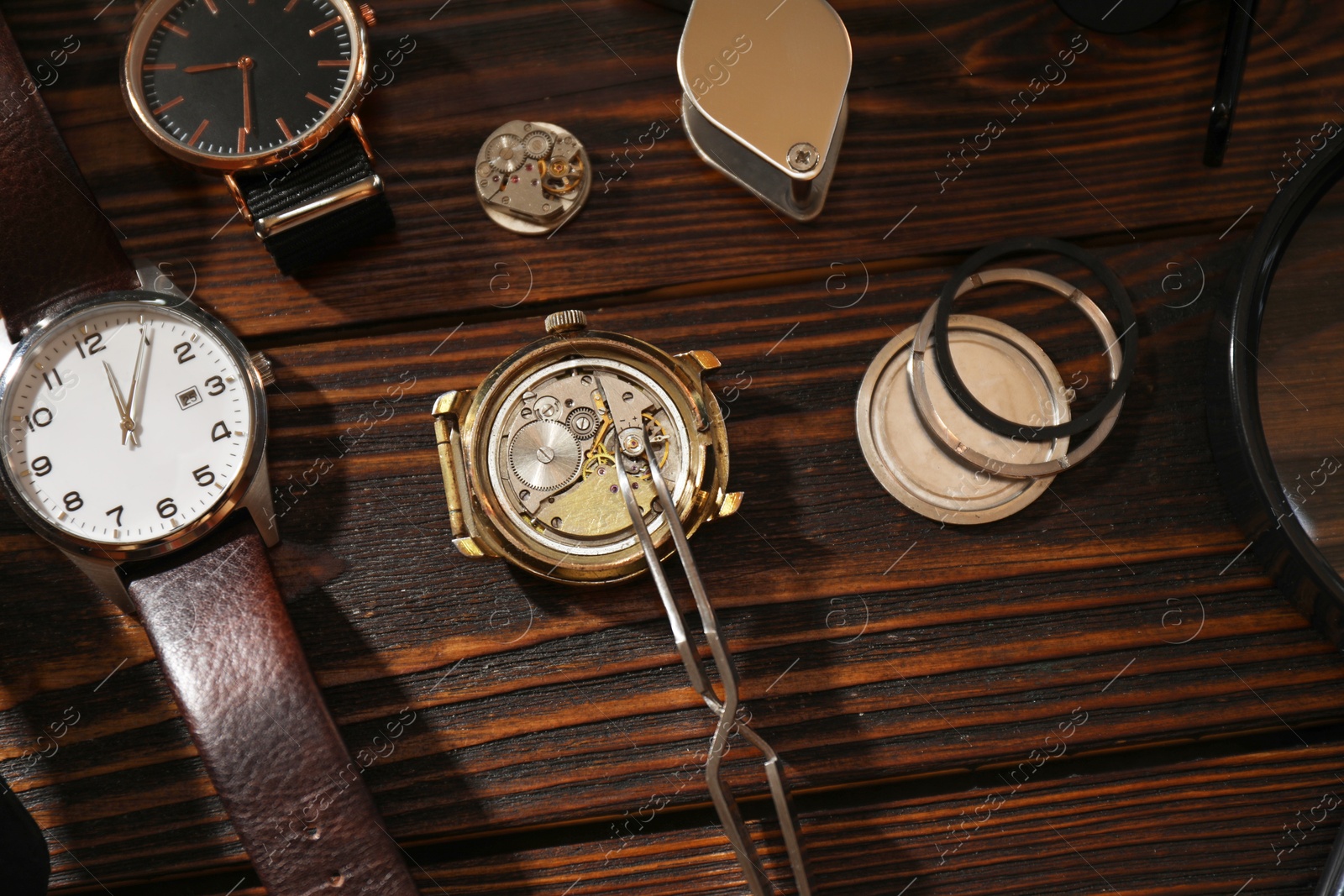 Photo of Clock mechanism. Different wrist watches and tool on wooden table, flat lay