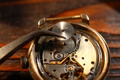 Mechanism of vintage wrist watch and tool on wooden table, closeup