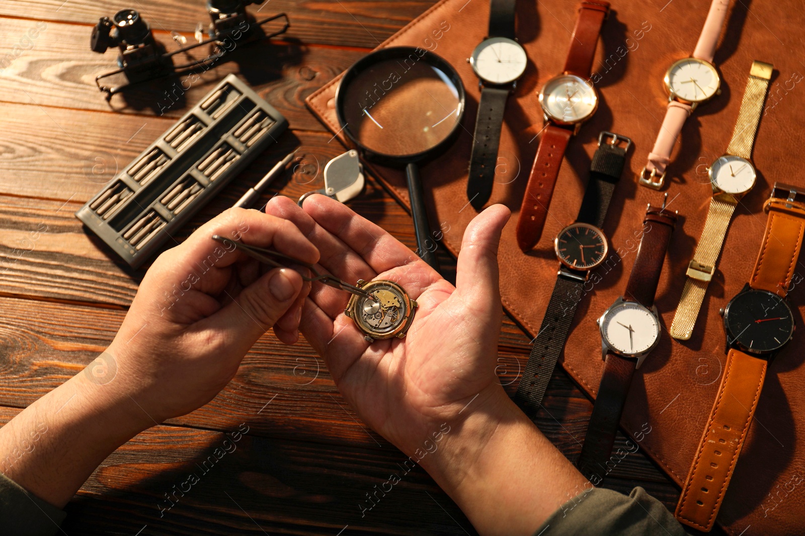 Photo of Man fixing mechanism of vintage wrist watch at wooden table, top view