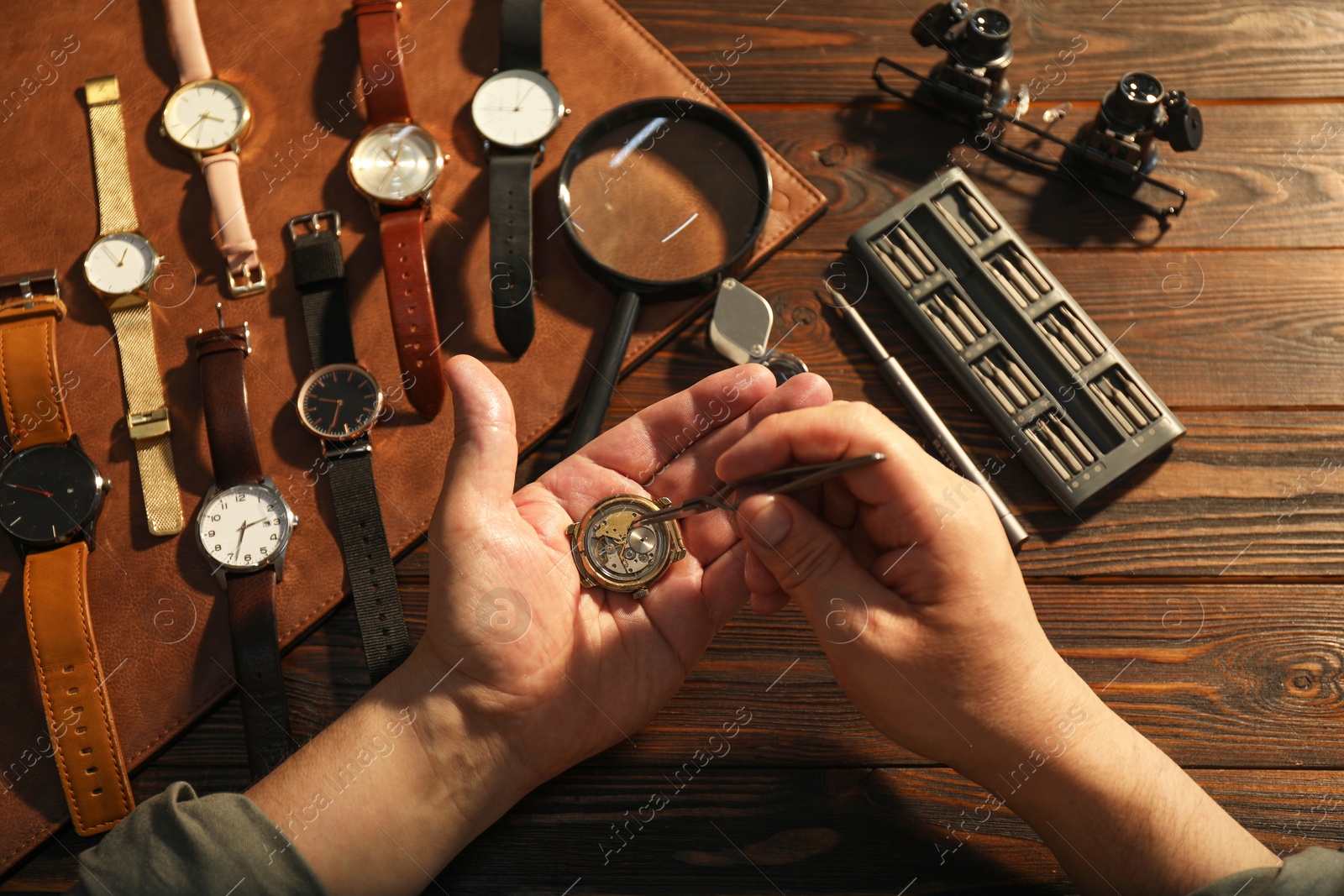 Photo of Man fixing mechanism of vintage wrist watch at wooden table, top view