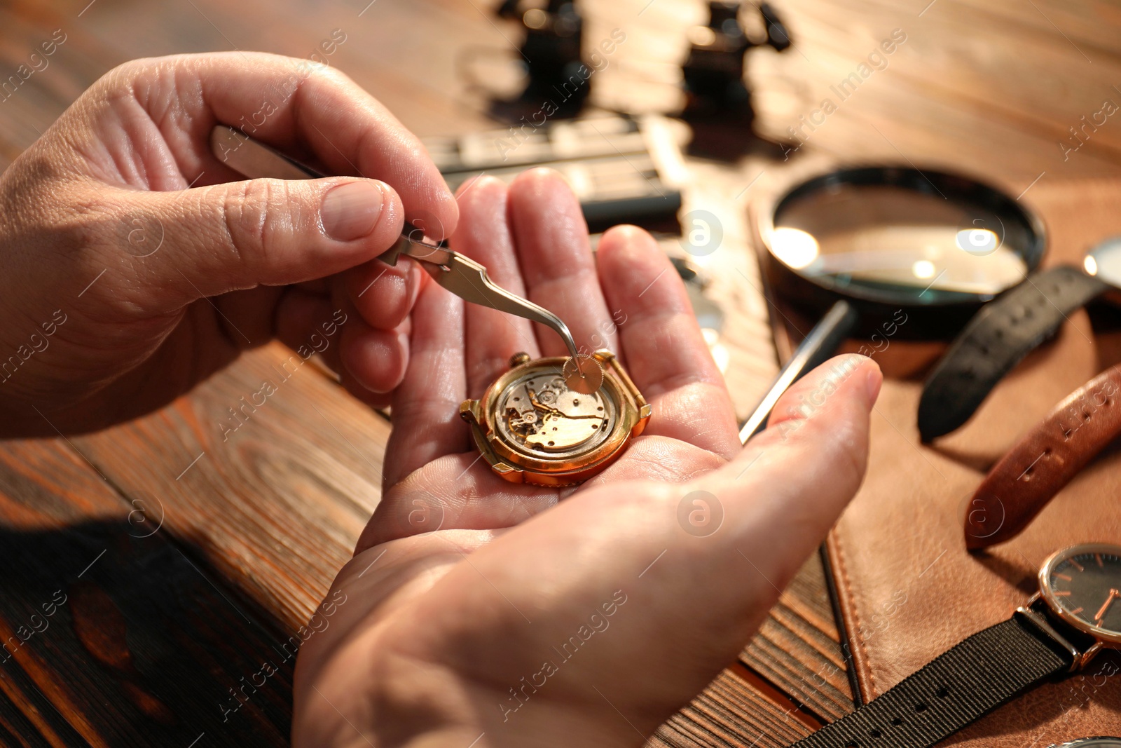 Photo of Man fixing mechanism of vintage wrist watch at wooden table, closeup