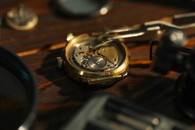 Photo of Mechanism of vintage wrist watch and tool on wooden table, closeup