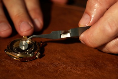 Photo of Man fixing mechanism of vintage wrist watch at table, closeup