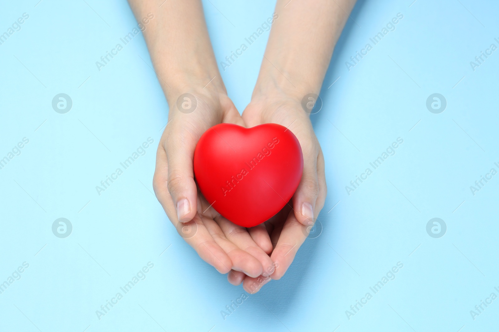 Photo of Woman holding red heart on light blue background, top view