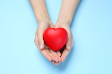 Photo of Woman holding red heart on light blue background, top view