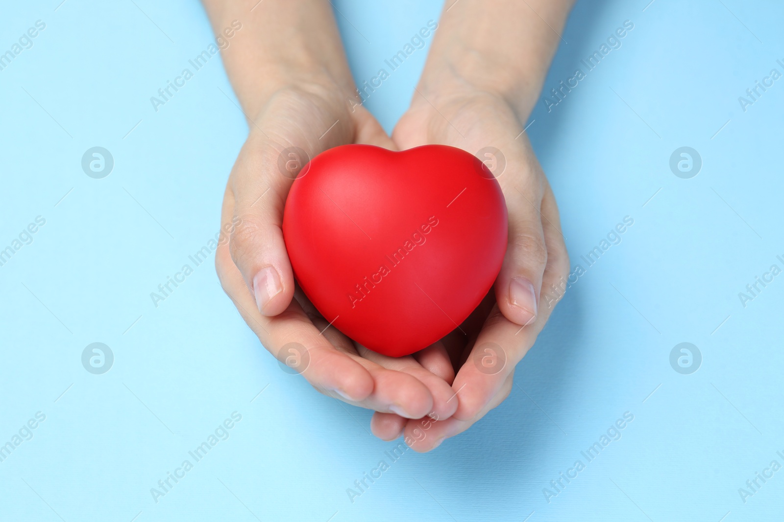 Photo of Woman holding red heart on light blue background, closeup