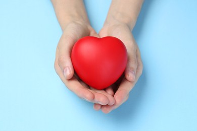 Woman holding red heart on light blue background, closeup