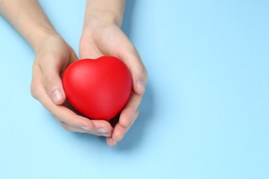 Woman holding red heart on light blue background, closeup. Space for text