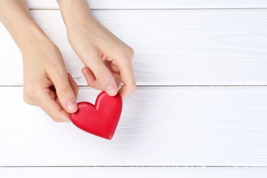 Photo of Woman holding red heart on white wooden background, top view. Space for text