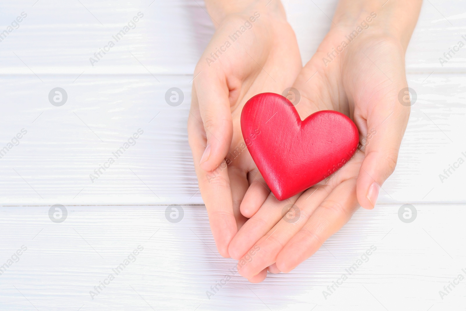 Photo of Woman holding red heart at white wooden table, closeup. Space for text