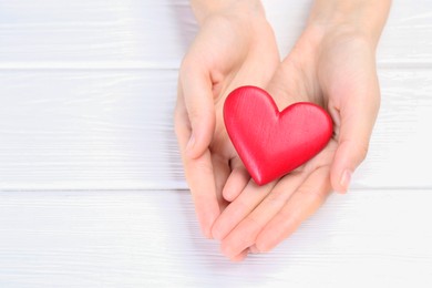 Photo of Woman holding red heart at white wooden table, closeup. Space for text